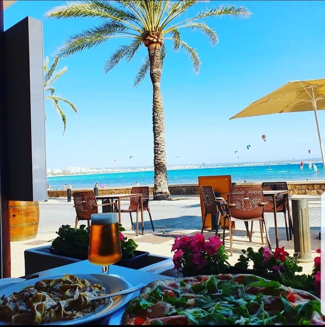 Terraza de Pizzería Eros frente al mar con palmera y pizza
